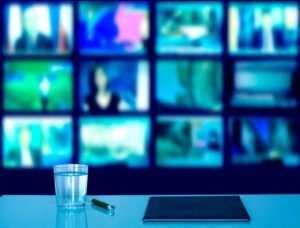 Bureau avec plusieurs écrans affichant un service IPTV, bloc-notes, stylo et verre d’eau 